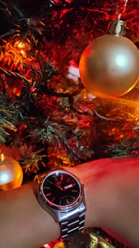 Cliente mostrando su reloj análogo Casio con esfera negra en la muñeca, con un árbol de Navidad de fondo.