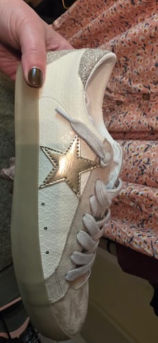 Customer holding a white PAULA sneaker, showing the gold star and silver glitter heel.