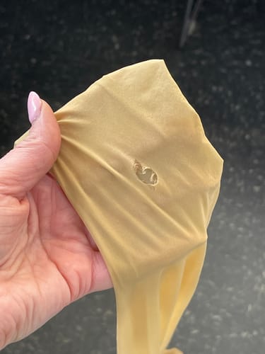 Reviewer's hand holding up the sheer tights to show a small hole in the fabric.