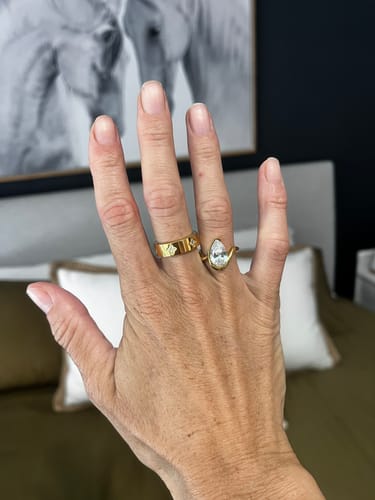 Reviewer's hand wearing the Lyric Ring, a gold ring with a large teardrop stone, on the middle finger.