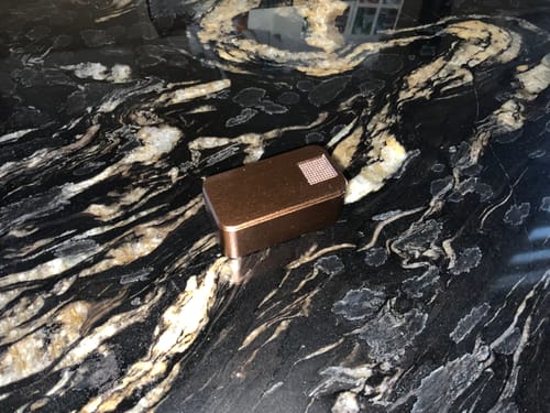 Customer's bronze-colored Nano Case resting on a black and gold marble countertop.