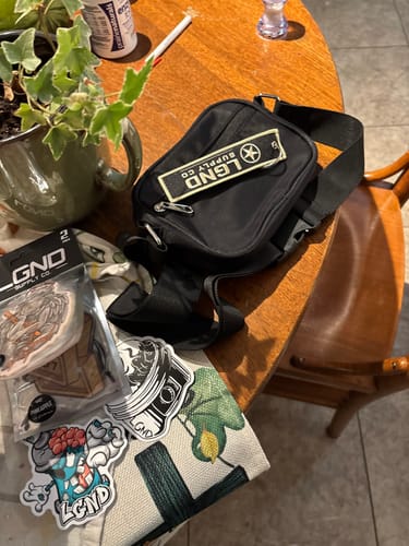 Customer's items from the Limited Overstock Drop, showing a black bag and several stickers on a wooden table.