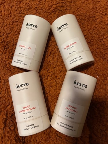 Reviewer's collection of four Aerre fragrances, including Smooth Jazz, in their white cylinder packaging on a brown surface.