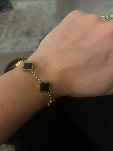 Customer wearing a gold-tone bracelet with black clover charms on their wrist.