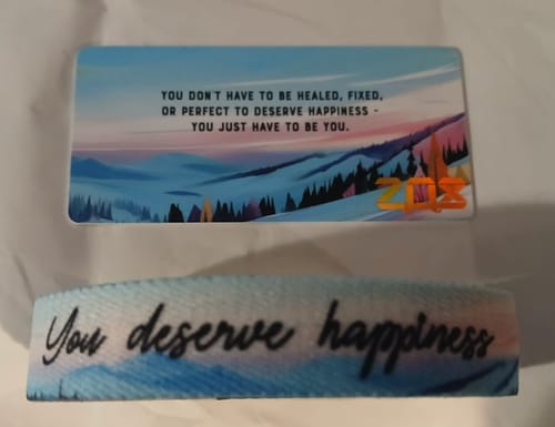 Customer's You Deserve Happiness Bracelet laid flat next to its matching collector's card with a mountain scene.