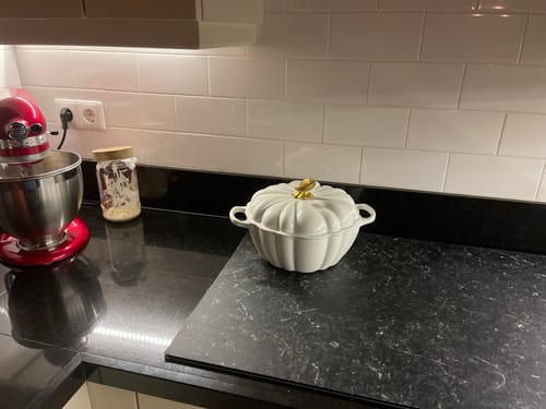 Recensent toont de witte Le Creuset Pompoen stoofpan op een donker aanrecht.