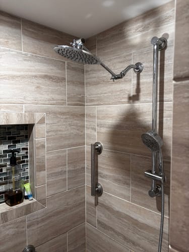 Customer's rain shower head and adjustable arm installed high in a tiled walk-in shower with grab bars.