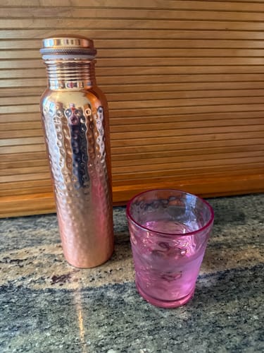 Customer's hand-hammered Pure Copper Water Bottle on a counter next to a glass of water.