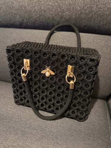 Customer's finished black Garden Bee Crochet Bag with a gold bee ornament sitting on a dark sofa.