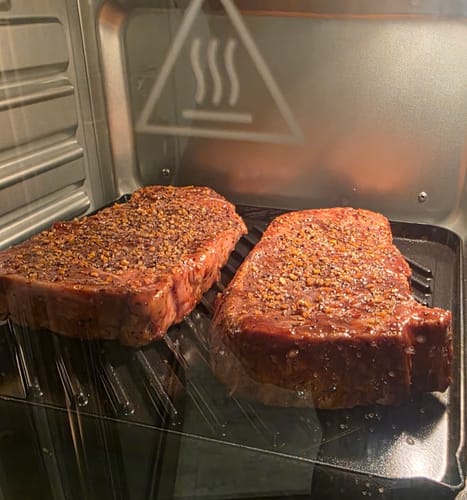 Reviewer's two seasoned raw steaks from the Steak Lover's Bundle on a grill pan inside an oven.