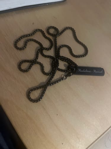 Reviewer's dark, engraved Odin necklace with the names 'Madalena - Manuel' on the pendant, lying on a wooden surface.