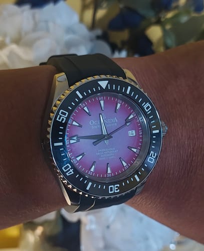 Customer's Oceaneva watch with a purple burst dial and black bezel, worn on their wrist.