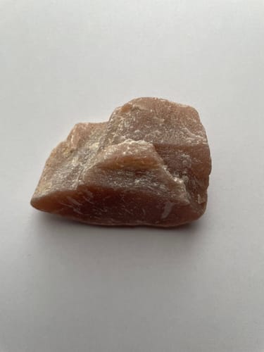 Photo d'un client montrant la pierre de lune pêche brute sur une surface blanche unie.