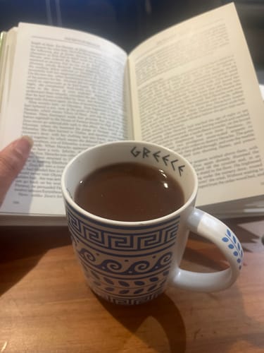 Customer's mug of Hot Chocolate on a wooden table next to an open book.