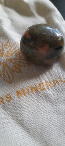 Un client montre sa pierre de Rhyolite polie et tachetée posée sur le pochon en tissu de la marque.