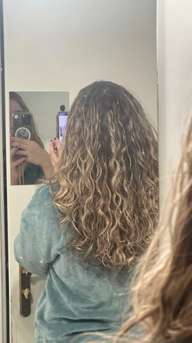Cliente de dos montrant ses longs cheveux blonds et ondulés, qui sont définis et volumineux grâce au Coffret Routine Curl Keeper.