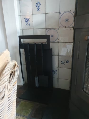 Het zwarte J-Line haardbestek van een recensent in de houder, staand naast een haard.