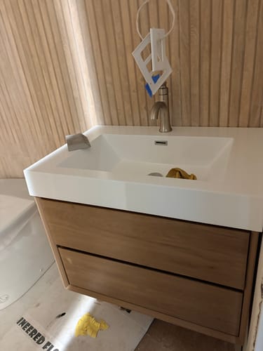 Customer's Maslow Floating Vanity with a wood finish and white sink top, shown during bathroom installation.