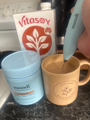 Customer preparing the Gingerbread blend in a tan mug, with the product tub and a carton of milk on the counter.