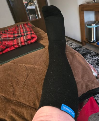 Customer's leg and foot wearing a black Performance Eucalyptus Compression Sock while resting indoors.