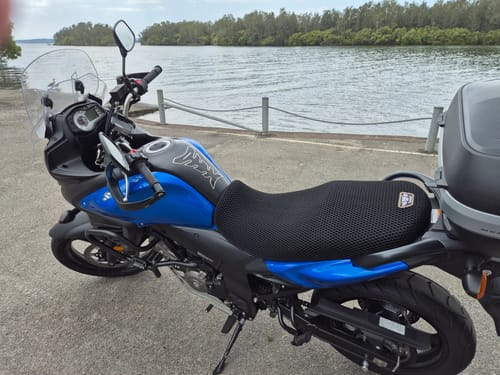 Customer's black Wind Rider Seat Cover fitted on a blue motorcycle parked near water.