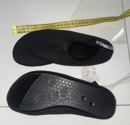 Customer's black Riot Deadlift Slippers, with one showing the textured sole and the other next to a measuring tape.