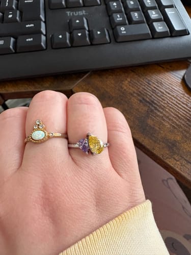 Close-up of a customer's hand wearing the Leesha Birthstone Ring with sparkly yellow and purple stones.