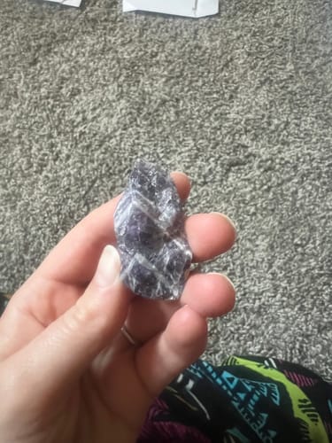 Close-up of a reviewer holding the raw Dream Amethyst crystal, showing its purple hue and white stripes.