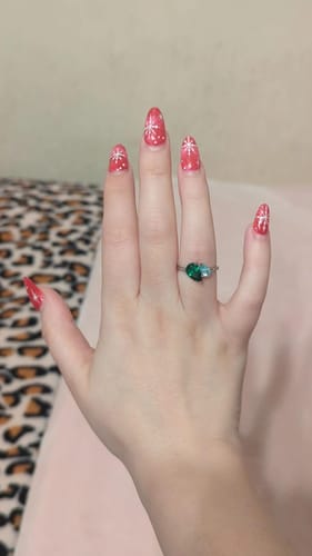 Customer wearing the Leesha Birthstone Ring with green and blue stones on their hand, which has festive nail art.