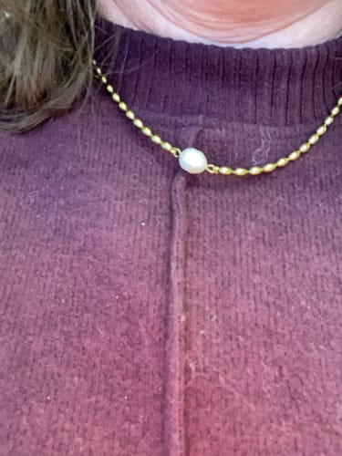 Close-up of a reviewer wearing the Pearl Necklace with a gold chain and single pearl.