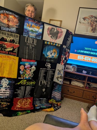 Reviewer happily holding up her large Premium T Shirt Quilt made from various dark concert t-shirts.