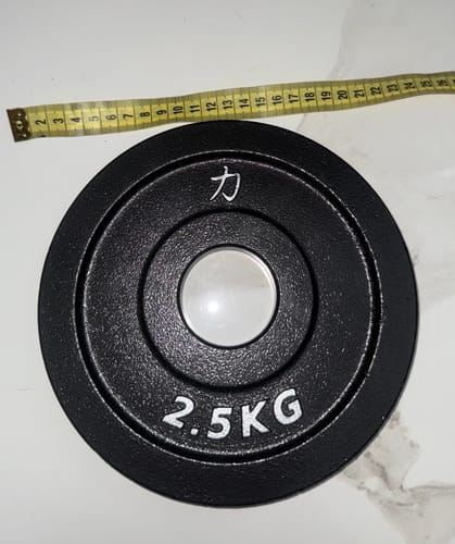Customer's black 2.5KG Riot Cast Iron Plate on a counter with a measuring tape verifying its size.