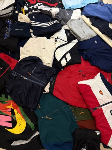 Customer's pile of colorful branded windbreakers, showing a variety of styles and logos from brands like Nike and Adidas.