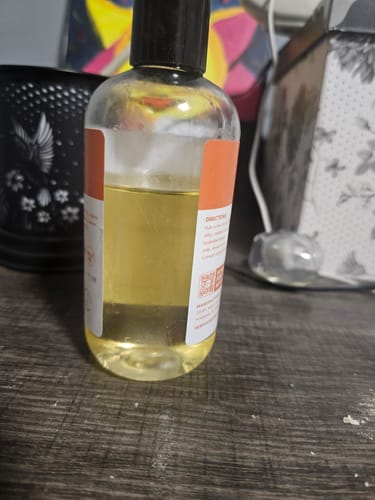 Customer's Skin Smoothing Body Oil in a clear bottle, half-full with golden liquid, on a surface.