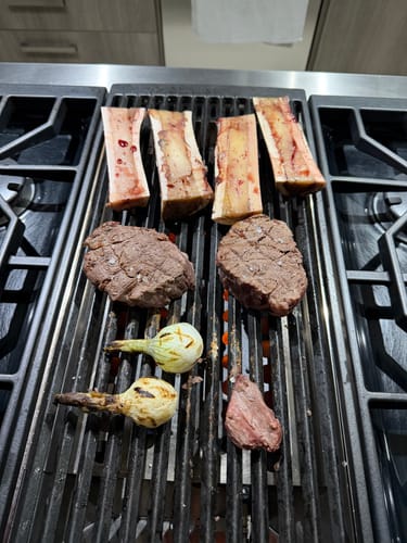 Cliente asando Hueso Tuetanero en Canoa en una parrilla con filetes de res y cebollas cambray.