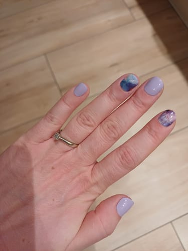 Kundin zeigt ihre Hand mit 'Pastel Petals' UV-Nagelfolien, kombiniert mit Nägeln in zartem Flieder.