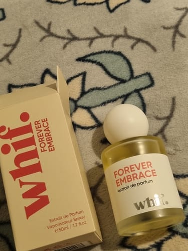 Reviewer's Forever Embrace perfume bottle and its cream-colored box on a floral surface.