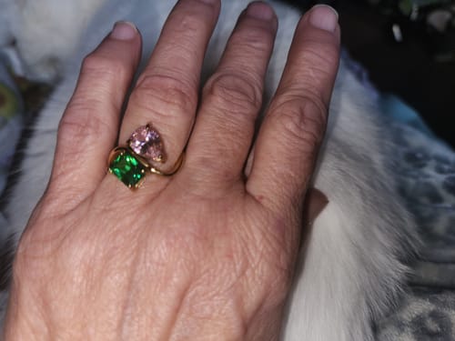 Customer's hand wearing the Navae Birthstone Ring with a large green radiant-cut and a pink pear-cut stone.