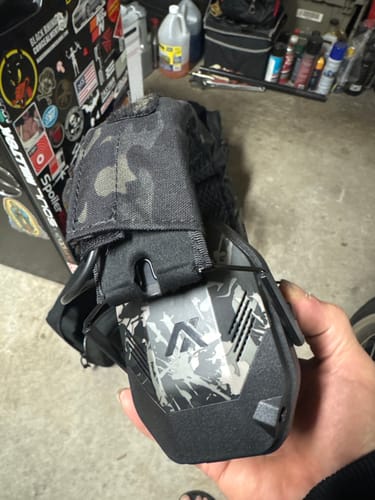 Reviewer's hand holding the MX PRO Earmuff Protection, showing its black and grey camouflage design.