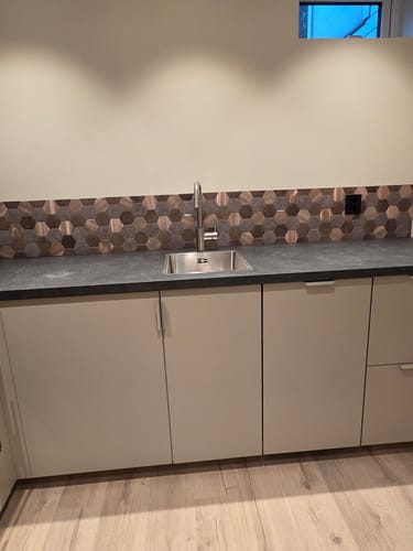 Kundens kjøkken med Bente hexagonfliser montert over en mørk benkeplate og beige skap.