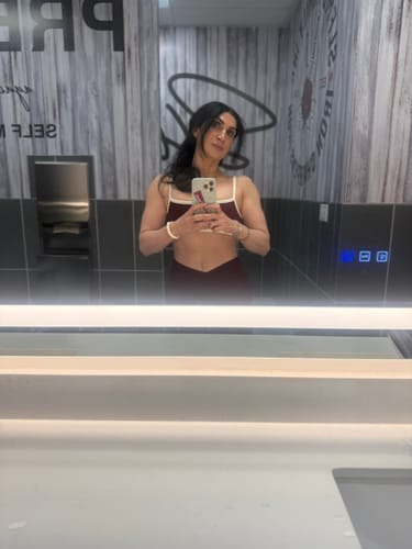 Reviewer takes a mirror selfie in a gym locker room, showing the front of the dark red The V Legging and matching bra.