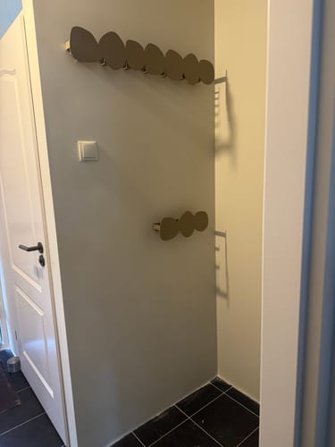 Recensent toont twee champagnekleurige Tumulo-wandkapstokken die boven elkaar aan een muur zijn gemonteerd.