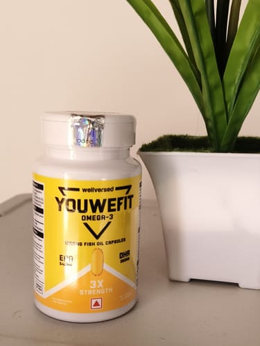 Customer's YouWeFit Omega-3 fish oil bottle with a yellow label, placed on a surface next to a potted plant.