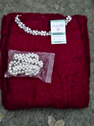 Clientul prezintă rochia Betta roșie din dantelă, împăturită, cu cureaua de perle vizibilă.