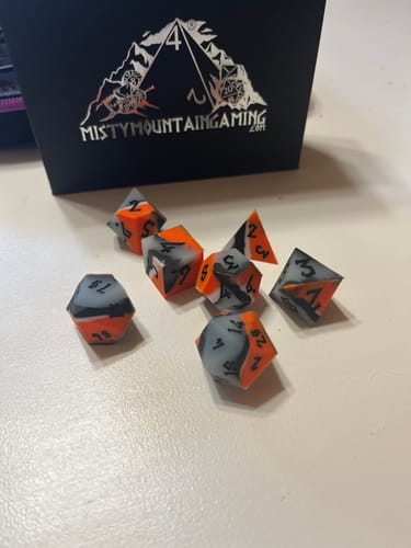 Customer's orange and gray Dark Matter Silicone Dice Set scattered on a table in front of the product's black box.