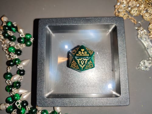Customer's personalized green D20 anniversary dice sitting in its black floating display case.
