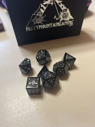 Customer's black Fangs of Winter Obsidian Stone Dice Set scattered on a table in front of the product box.