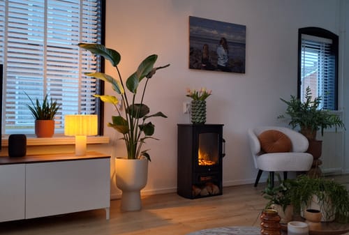 Klant toont de witte Elho Vibes Fold Coupe bloempot met een grote plant erin, in een sfeervol ingerichte woonkamer.