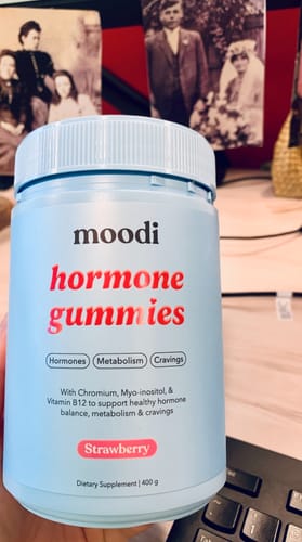 Reviewer holding the light blue bottle of Strawberry Hormone Gummies at a desk.