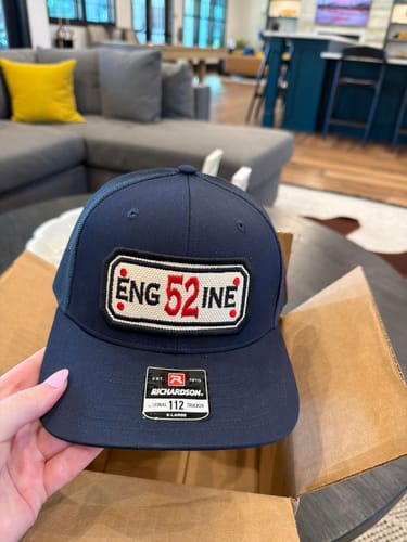 Customer holding their newly unboxed navy blue Snapback Hose Hat in their home.